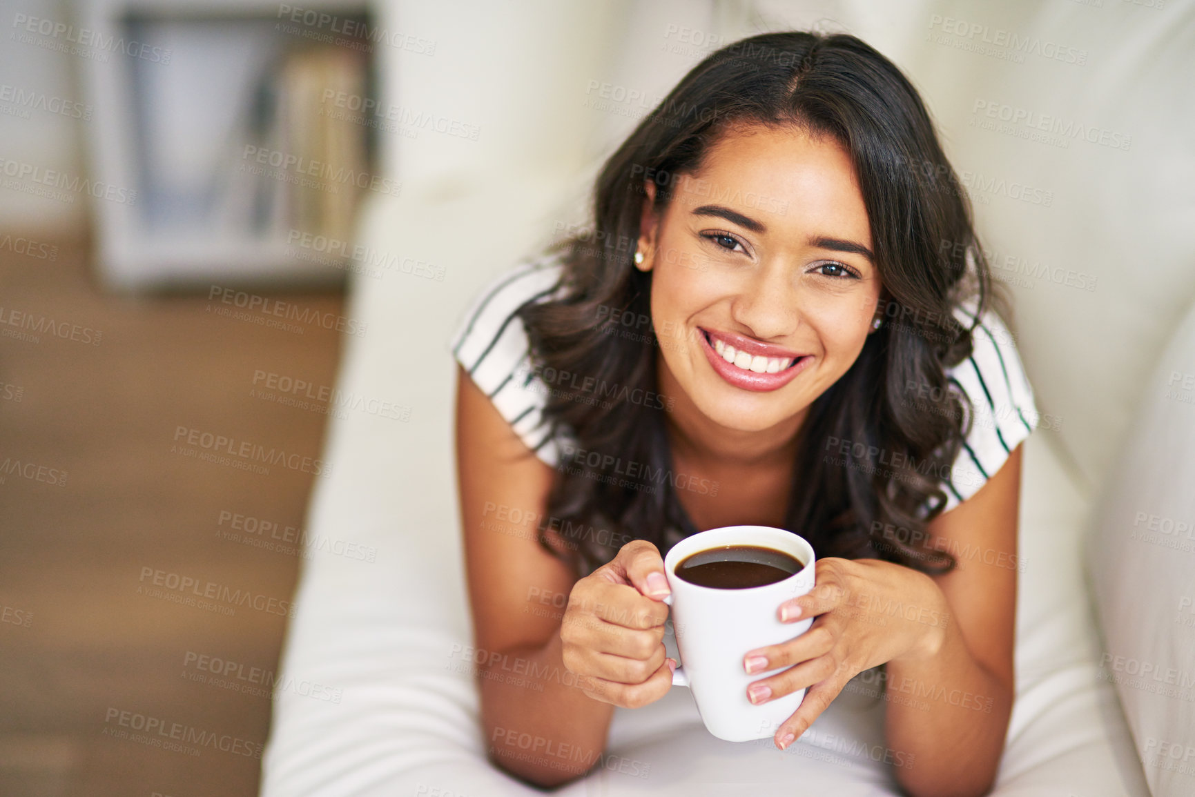 Buy stock photo Cropped portrait of a young woman drinking coffee while relaxing on her sofa at home