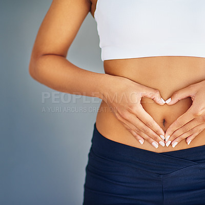 Buy stock photo Cropped shot of a young woman making a heart shape on her stomach