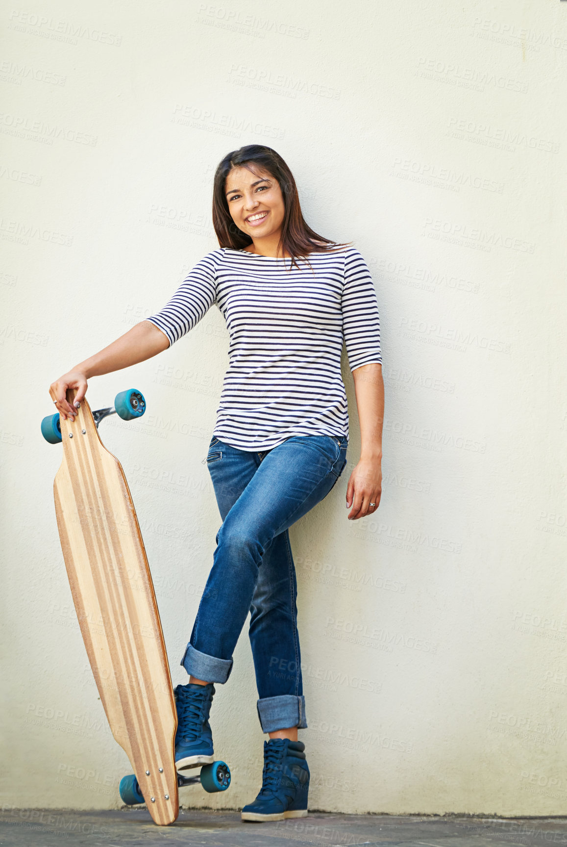 Buy stock photo Shot of a young skater standing against a wall with her longboard