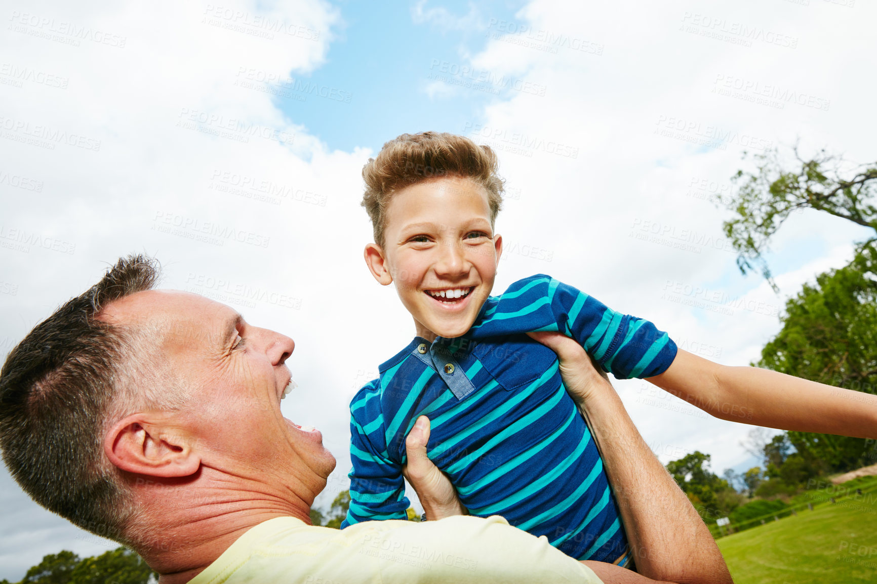 Buy stock photo Shot of a dad standing outside holding his son up in the air