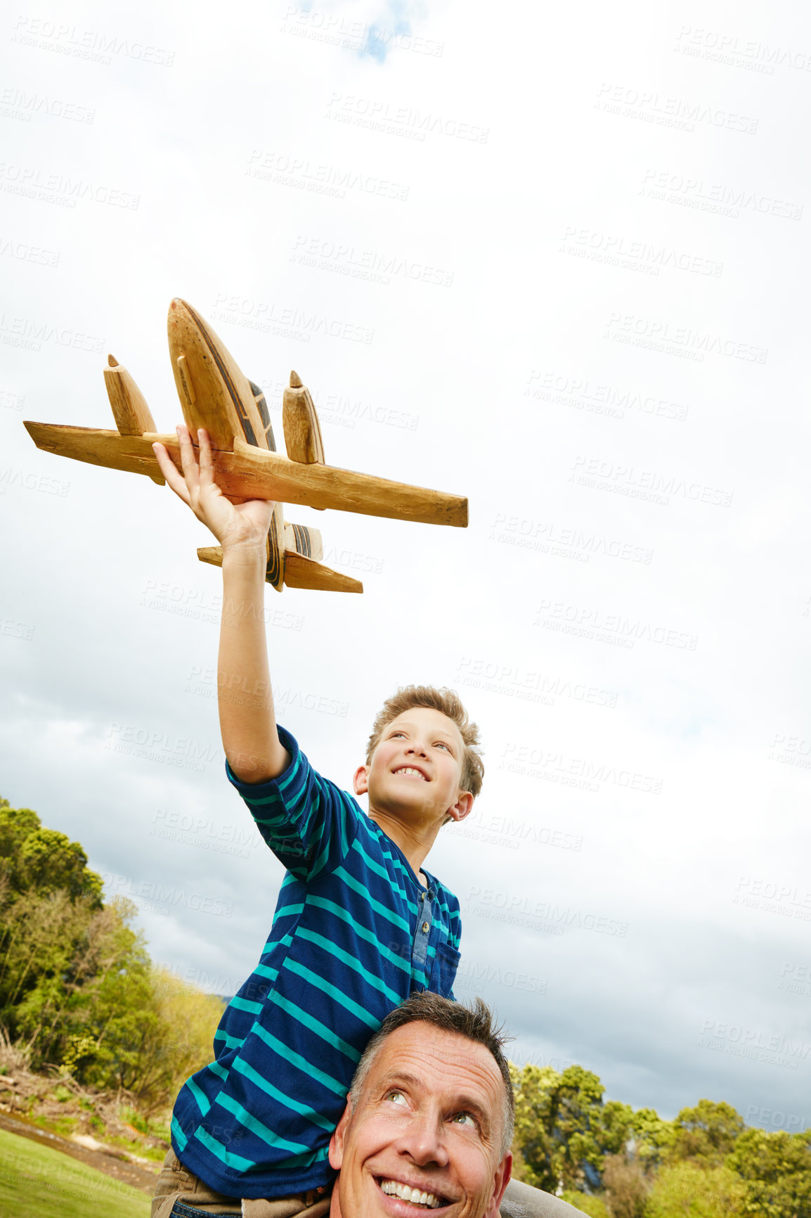 Buy stock photo Shot of a boy playing with a toy airplane while getting a piggyback from his father outside