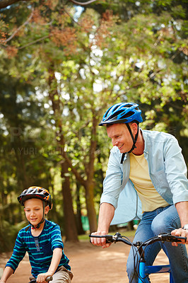 Buy stock photo Shot of a father and his young son riding bicycles through a park