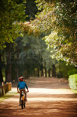 Buy stock photo Rearview shot of a little boy riding a bicycle through a park
