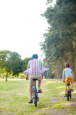 Buy stock photo Rearview shot of a father and son riding bicycles in a park