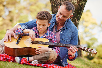 Buy stock photo Shot of a father teaching his son how to play guitar while sitting outside