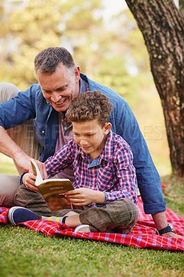 Buy stock photo Shot of a father and son reading a book together in a park