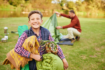 Buy stock photo Portrait of a young boy holding camping gear with his father in the background