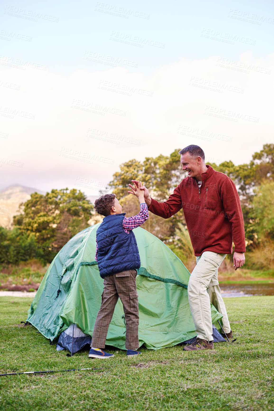 Buy stock photo Shot of a father and son hi fiving after setting up a tent together while camping