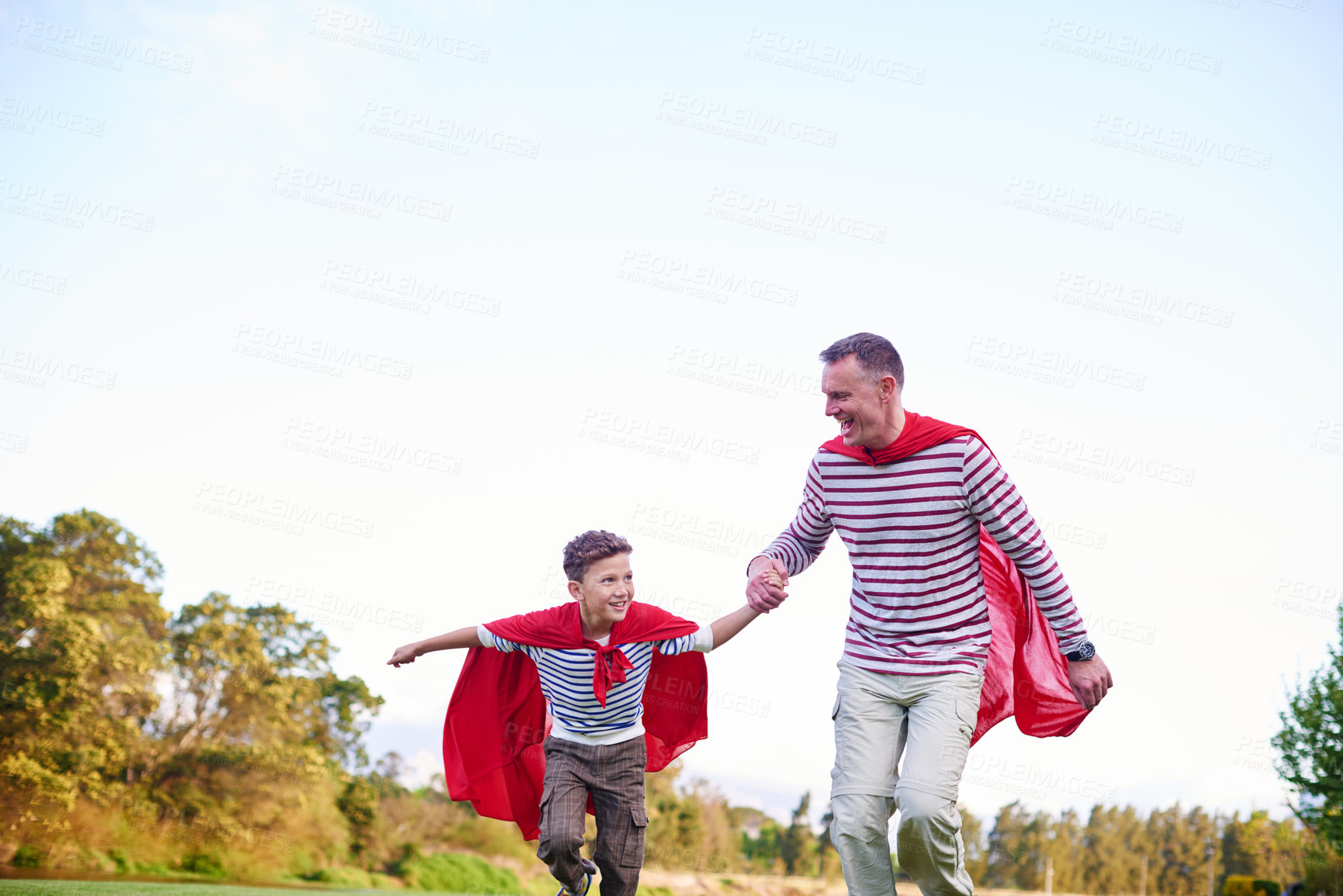Buy stock photo Shot of a father and his young son pretending to be superheroes while playing outdoors