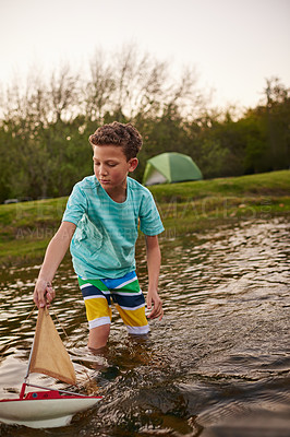 Buy stock photo Shot of a young boy standing in a lake playing with a toy boat