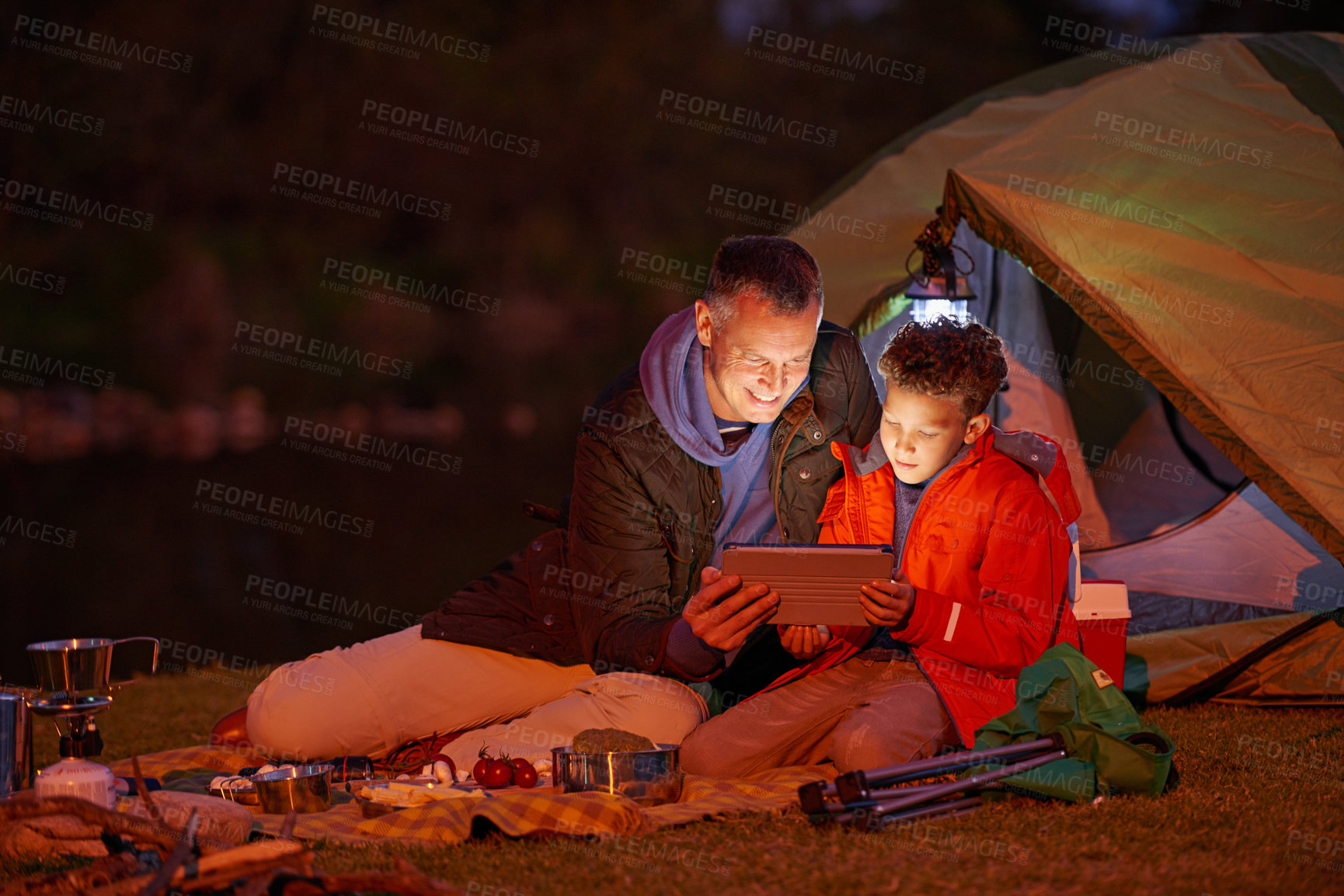 Buy stock photo Shot of a father and son watching a movie on a digital tablet while camping