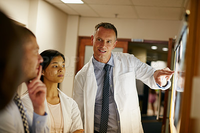 Buy stock photo Shot of a team of surgeons discussing a patient’s medical scans