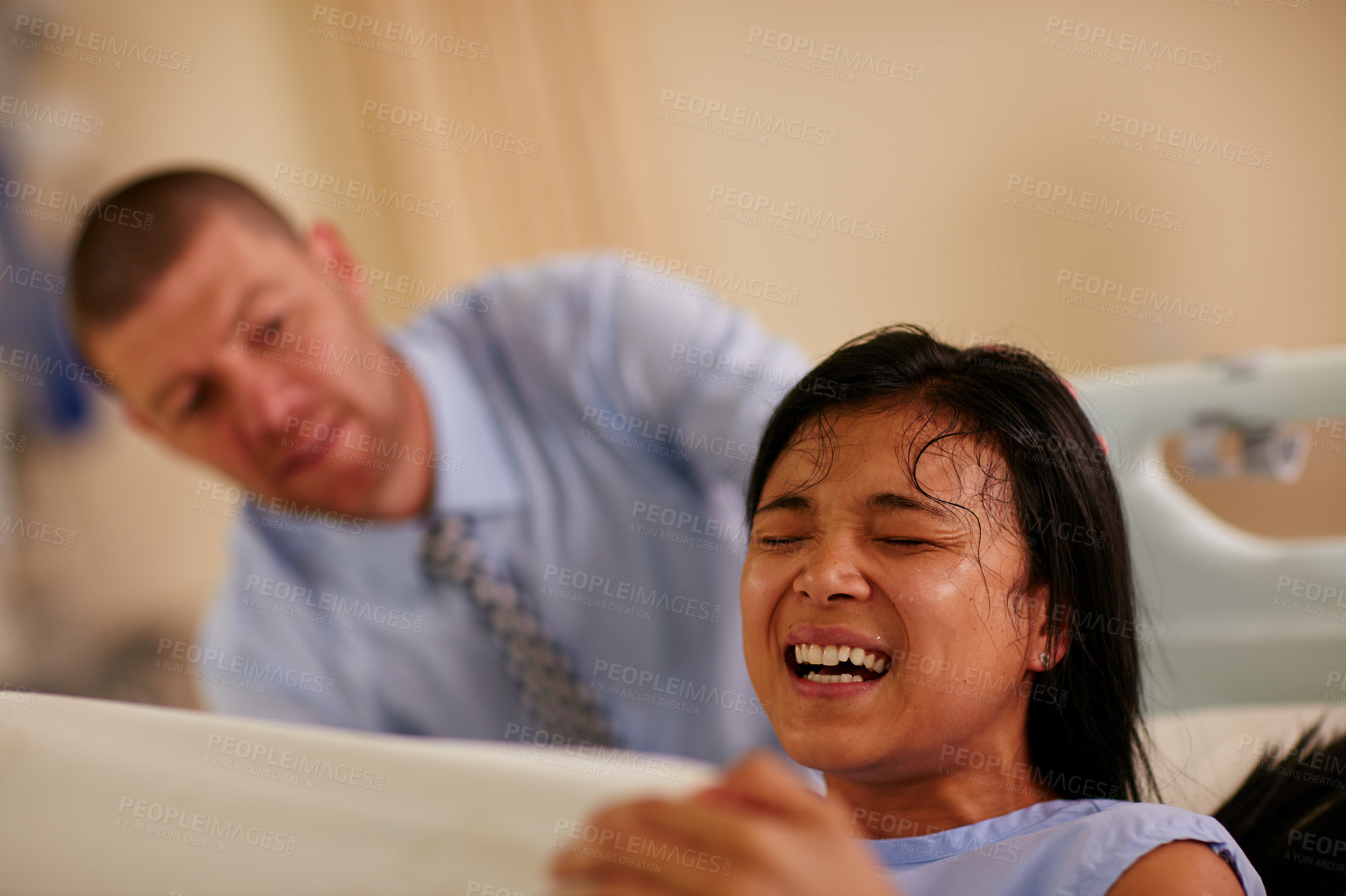 Buy stock photo Shot of a young woman giving birth with her husband supporting her in the background