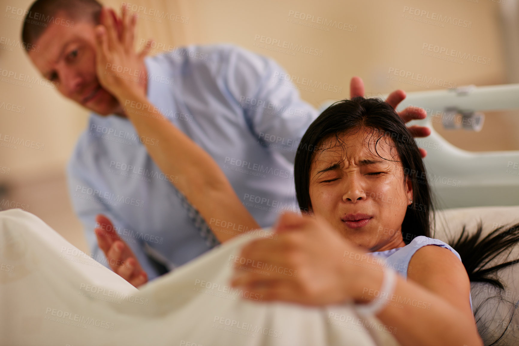 Buy stock photo Shot of a young woman giving birth with her husband supporting her in the background