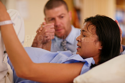 Buy stock photo Shot of a young woman giving birth with her husband supporting her in the background
