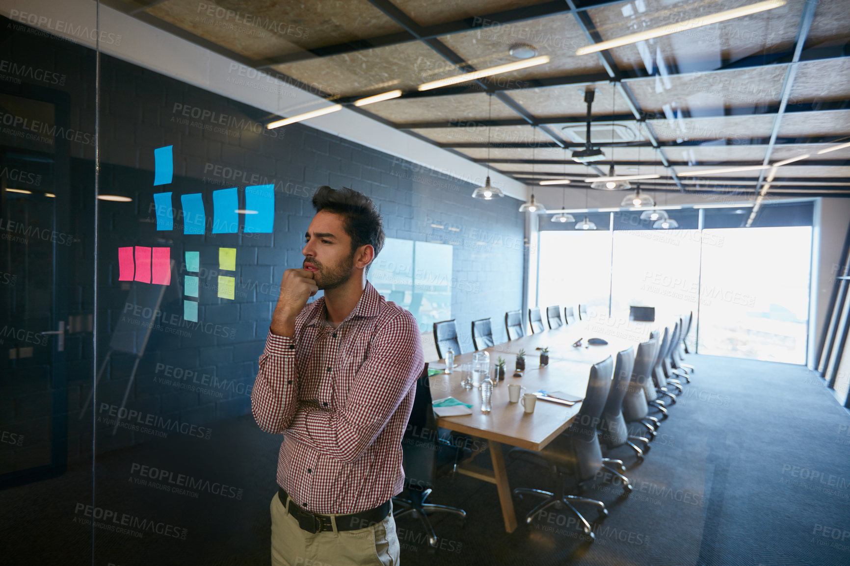 Buy stock photo Shot of a young businessman looking at sticky notes on a glass wall