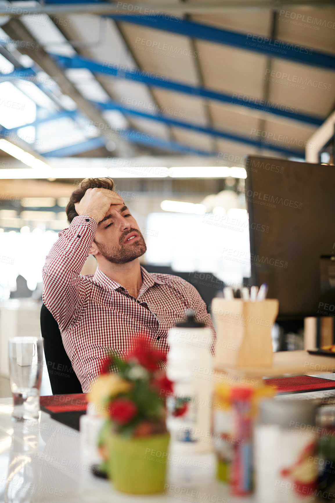 Buy stock photo Shot of a young businessman looking stressed while sitting at his desk