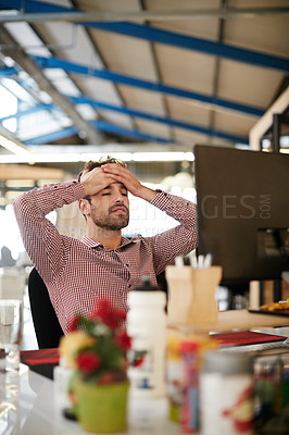 Buy stock photo Shot of a young businessman looking stressed while sitting at his desk