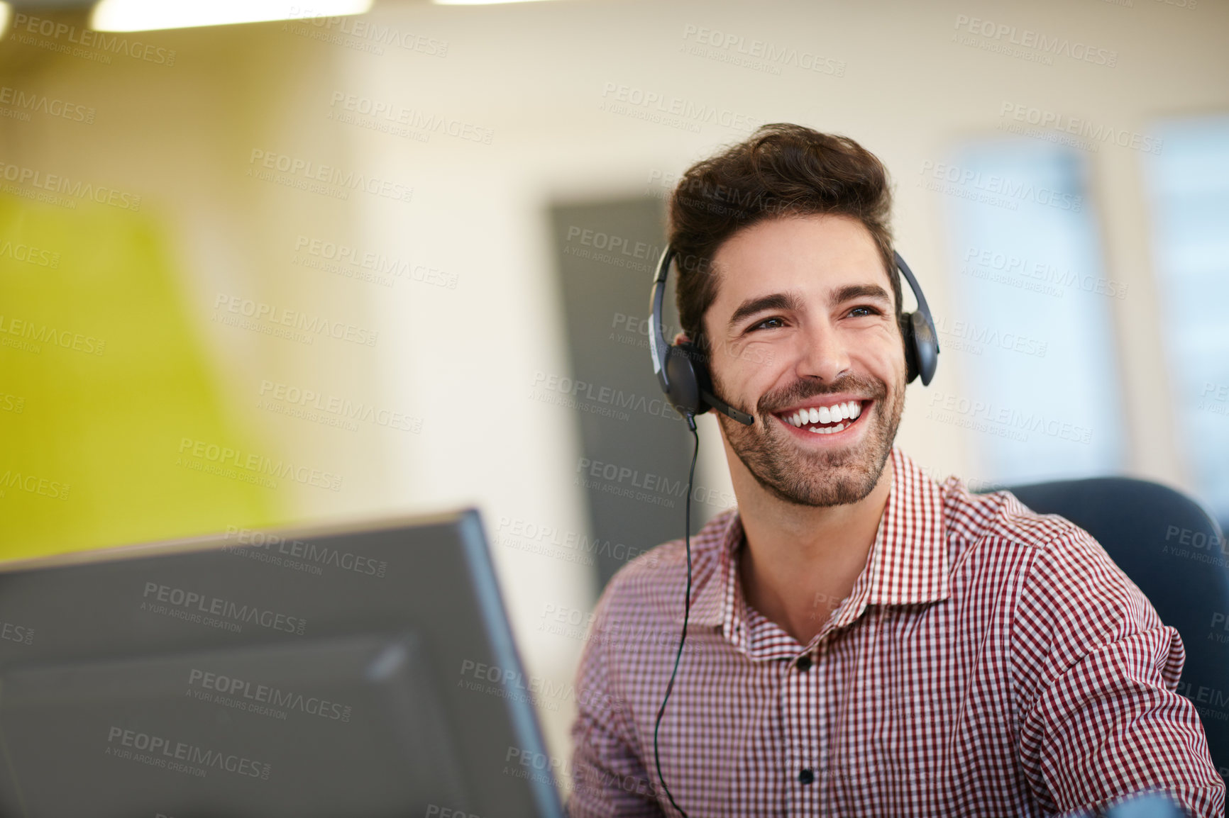 Buy stock photo Shot of a friendly young call centre agent sitting at his desk