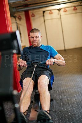 Buy stock photo Full length shot of a young man working out on the rowing machine at the gym
