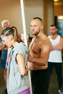 Buy stock photo Shot of a young woman doing pvc pipe exercises with the assistance of her trainer