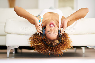 Buy stock photo Shot of a young woman listening to music while lying upside down on her couch