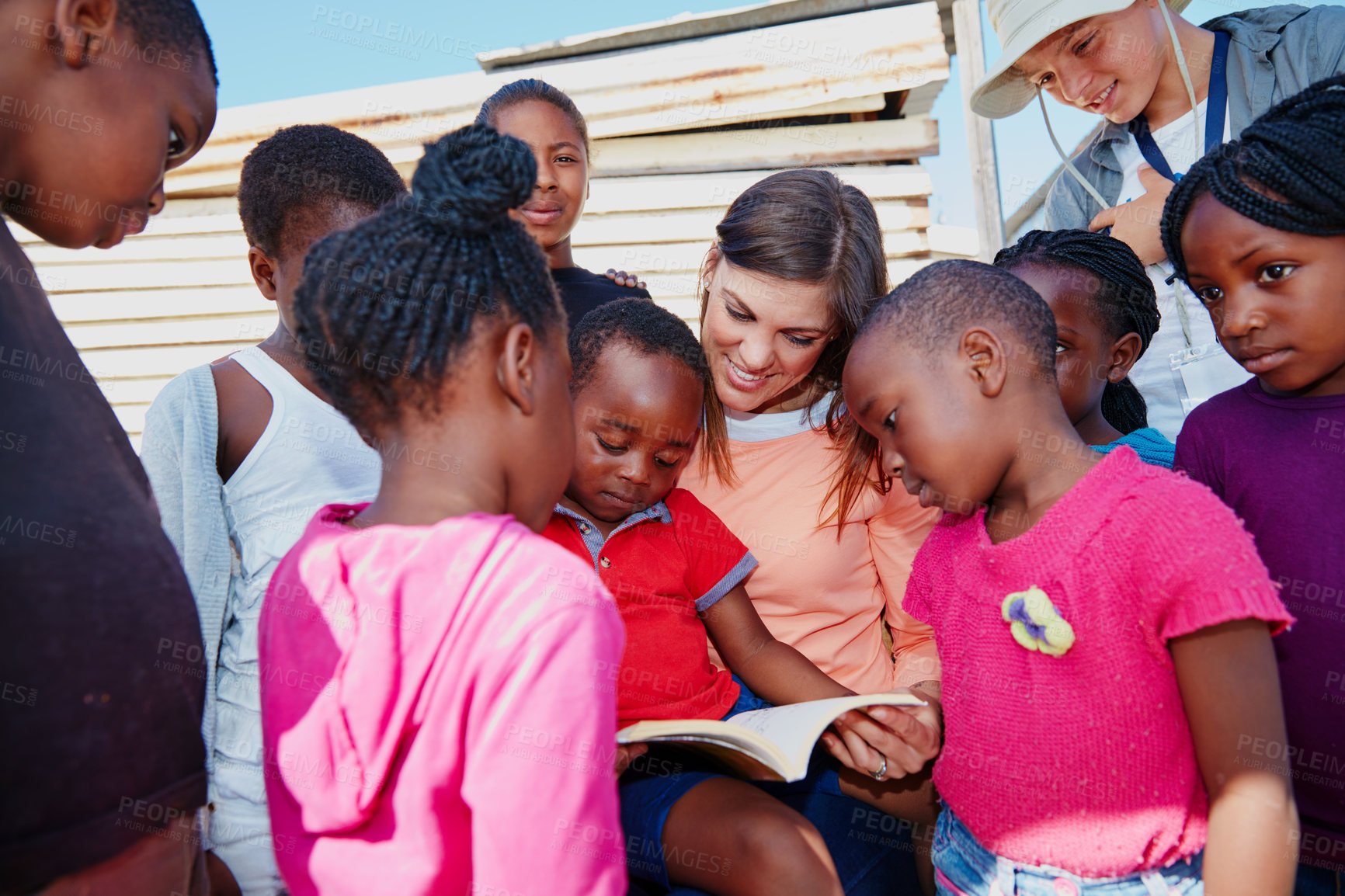 Buy stock photo Cropped shot of a volunteer worker reading to a group of children at a community outreach event