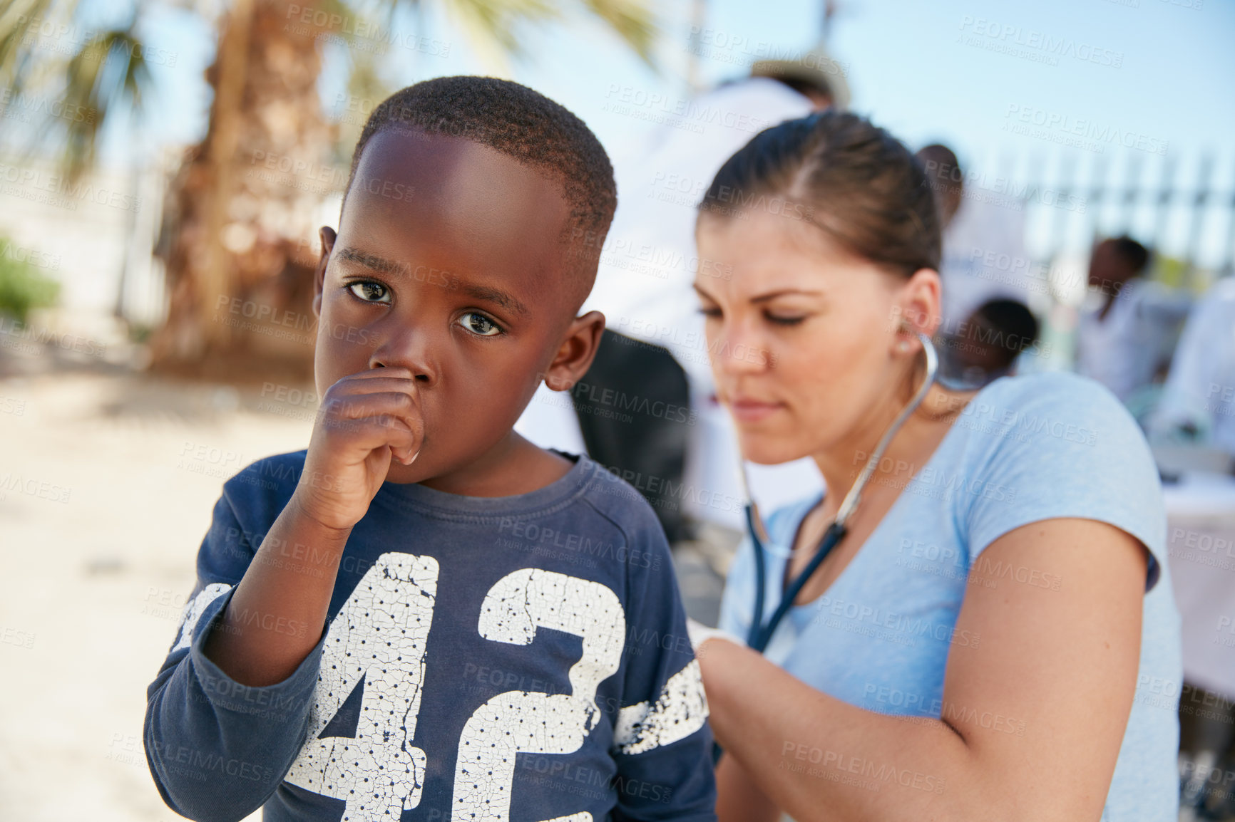 Buy stock photo Shot of a volunteer nurse examining a young patient with a stethoscope at a charity event