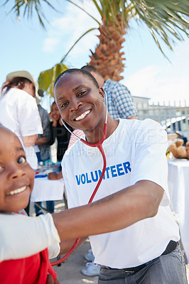 Buy stock photo Shot of a volunteer doctor examining a young patient with a stethoscope at a charity event