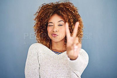 Buy stock photo Happy woman, portrait and wink with peace sign for cool attitude, beauty or style on a blue studio background. Young, female person or hipster model with pout, finger gesture or kiss in casual jersey