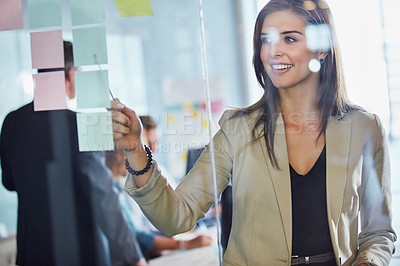 Buy stock photo Shot of a businesswoman arranging sticky notes on a glass wall during a brainstorming session