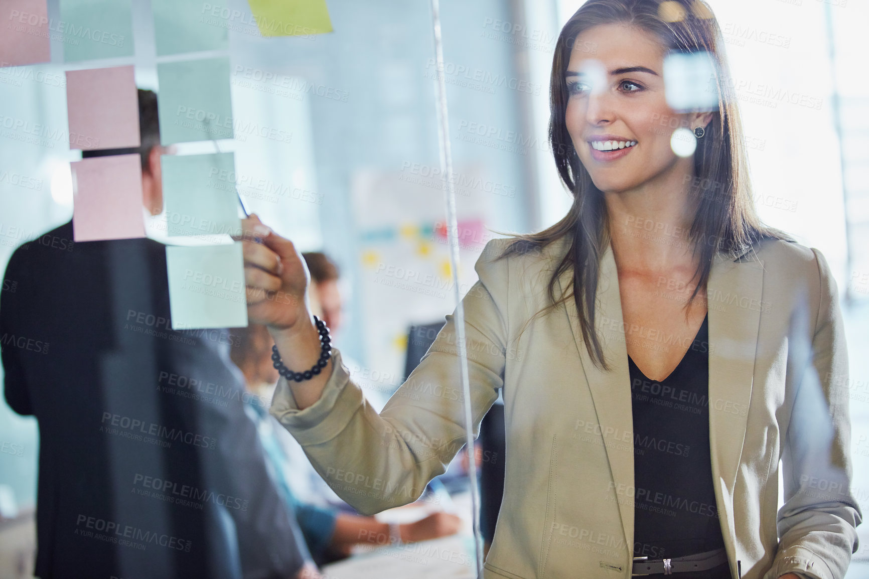 Buy stock photo Shot of a businesswoman arranging sticky notes on a glass wall during a brainstorming session