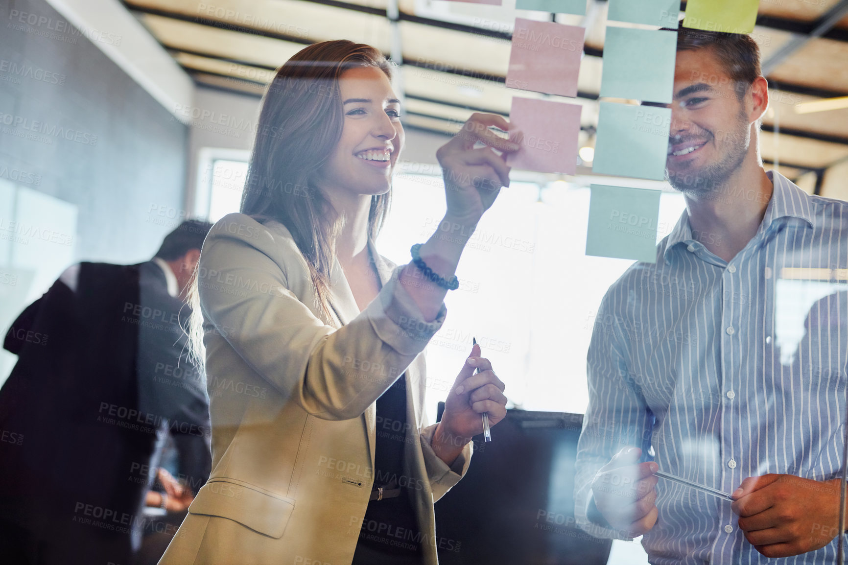 Buy stock photo Shot of coworkers arranging sticky notes on a glass wall during a brainstorming session