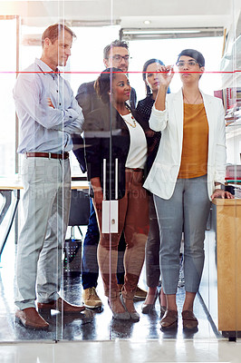 Buy stock photo Full length shot of a businesswoman writing on a glass wall while her colleagues look on