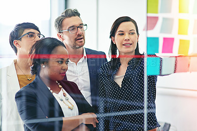 Buy stock photo Cropped shot of a businesswoman pointing out something on a glass wall while her colleagues look on