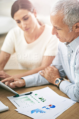Buy stock photo Shot of two coworkers sitting at a table discussing paperwork while using a digital tablet