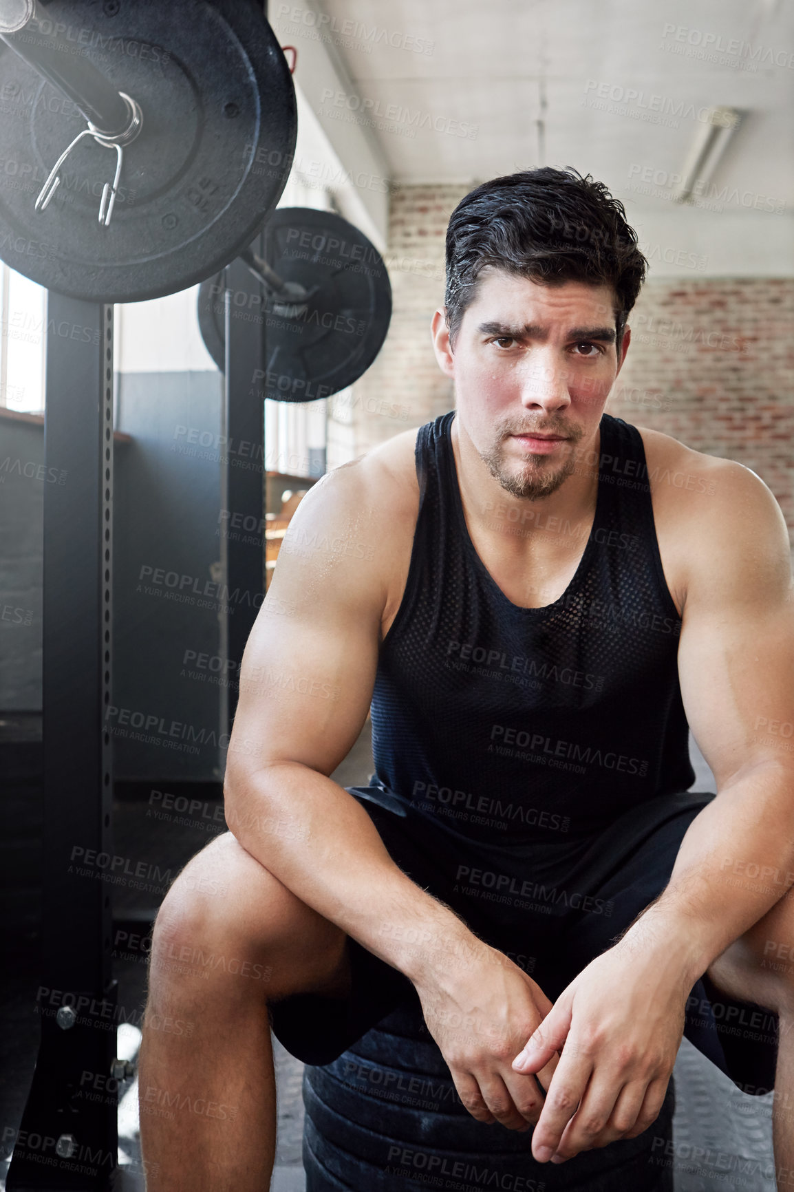 Buy stock photo Shot of a young man taking a break from working out with weights in the gym