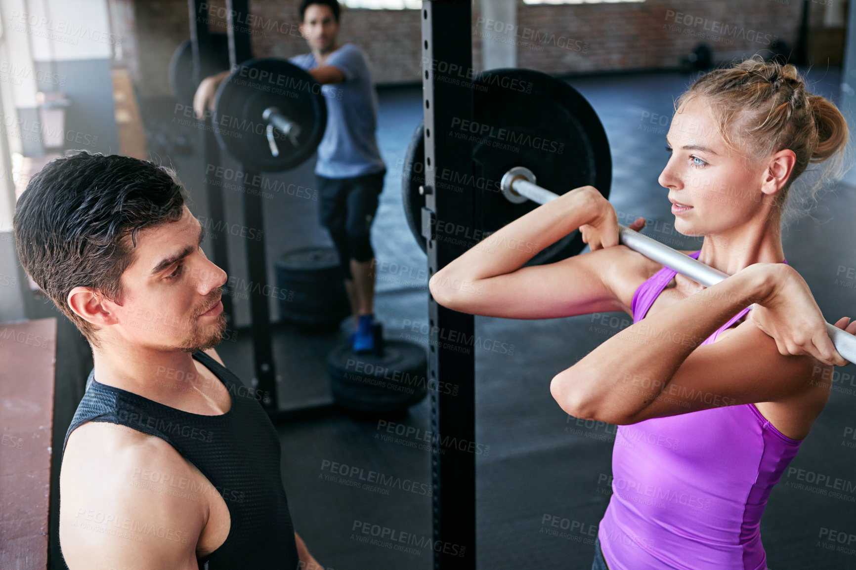 Buy stock photo Shot of a young woman lifting weights with her personal trainer assisting her