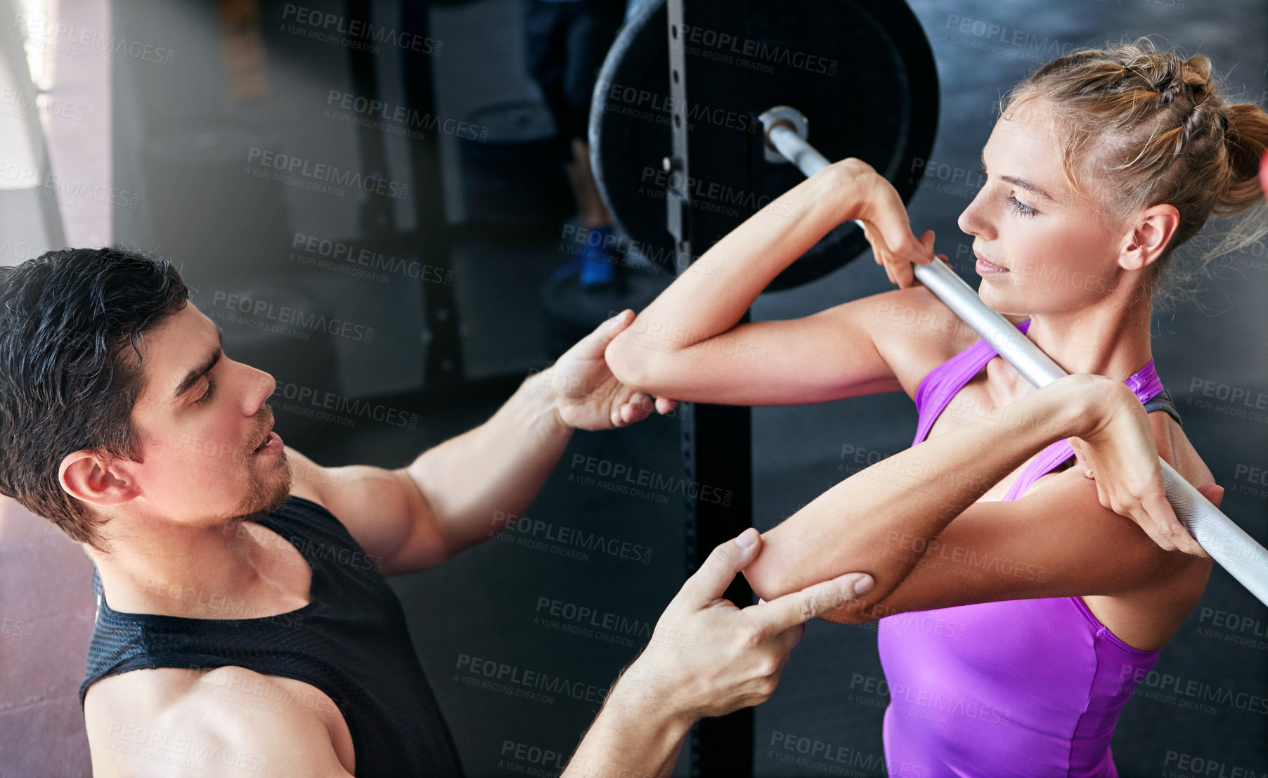 Buy stock photo Shot of a young woman lifting weights with her personal trainer assisting her