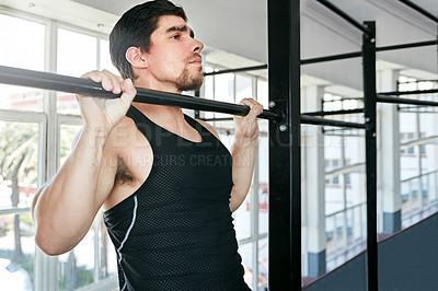 Buy stock photo Shot of a young man doing pull ups in a gym