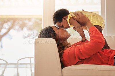 Buy stock photo Shot of a mother holding up her baby while lying on her sofa at home