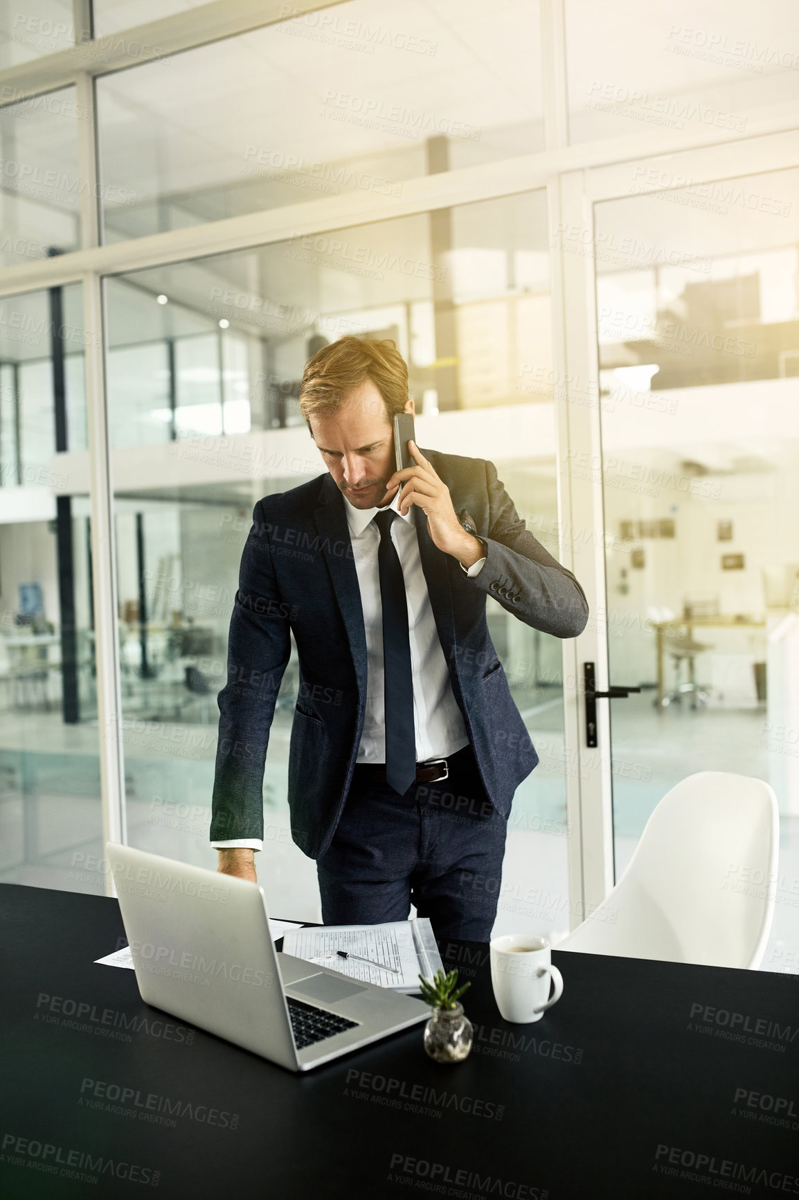 Buy stock photo Shot of a businessman talking on his cellphone while using his laptop