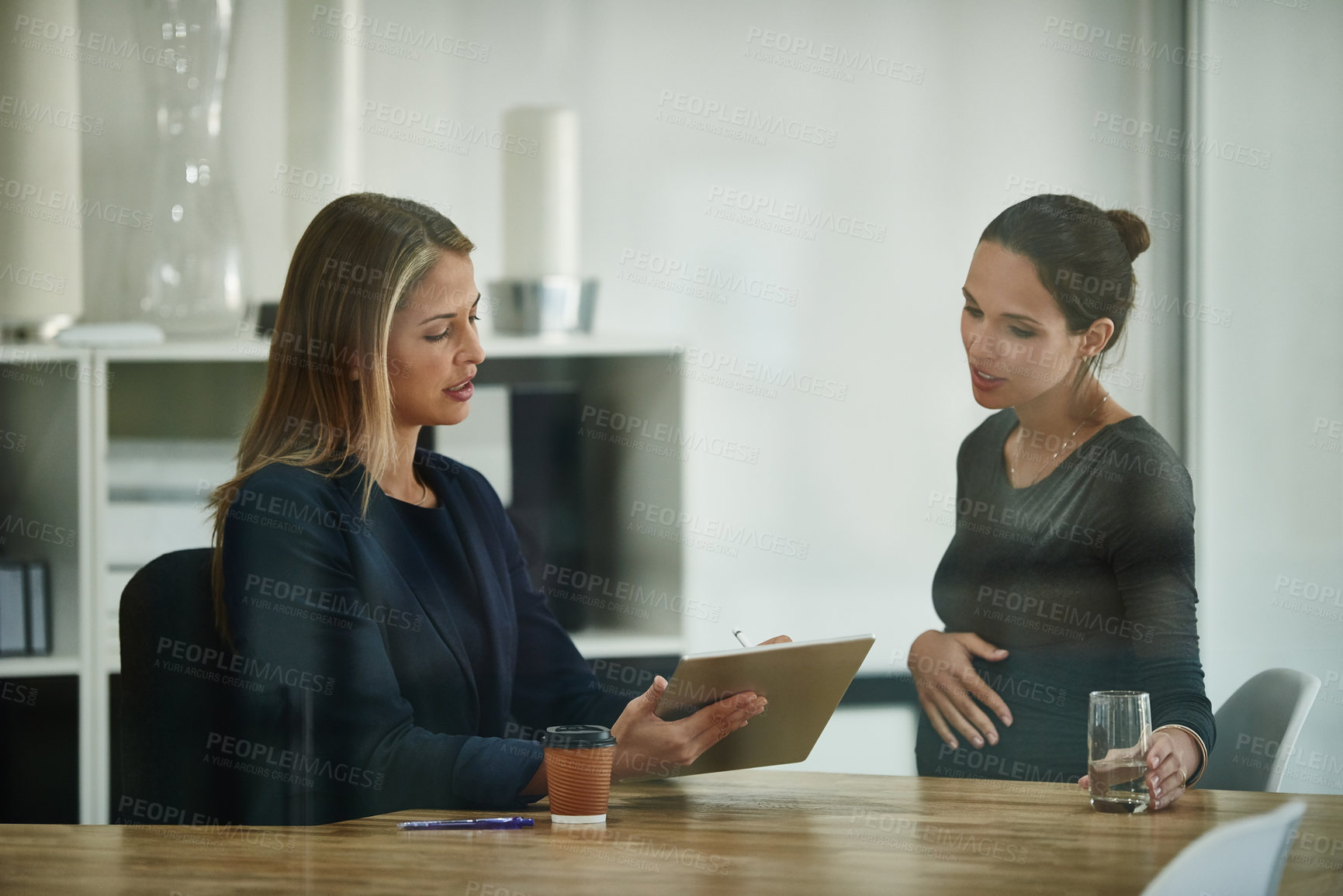 Buy stock photo Shot of a pregnant businesswoman and a colleague using a digital tablet together in an office