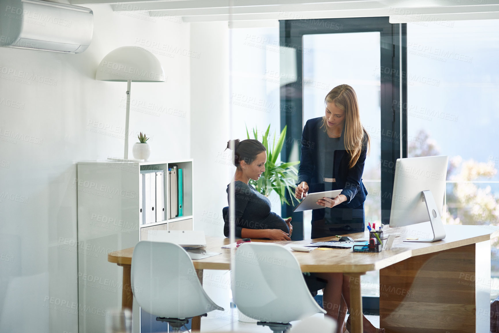 Buy stock photo Shot of a pregnant businesswoman and a colleague using a digital tablet together in an office