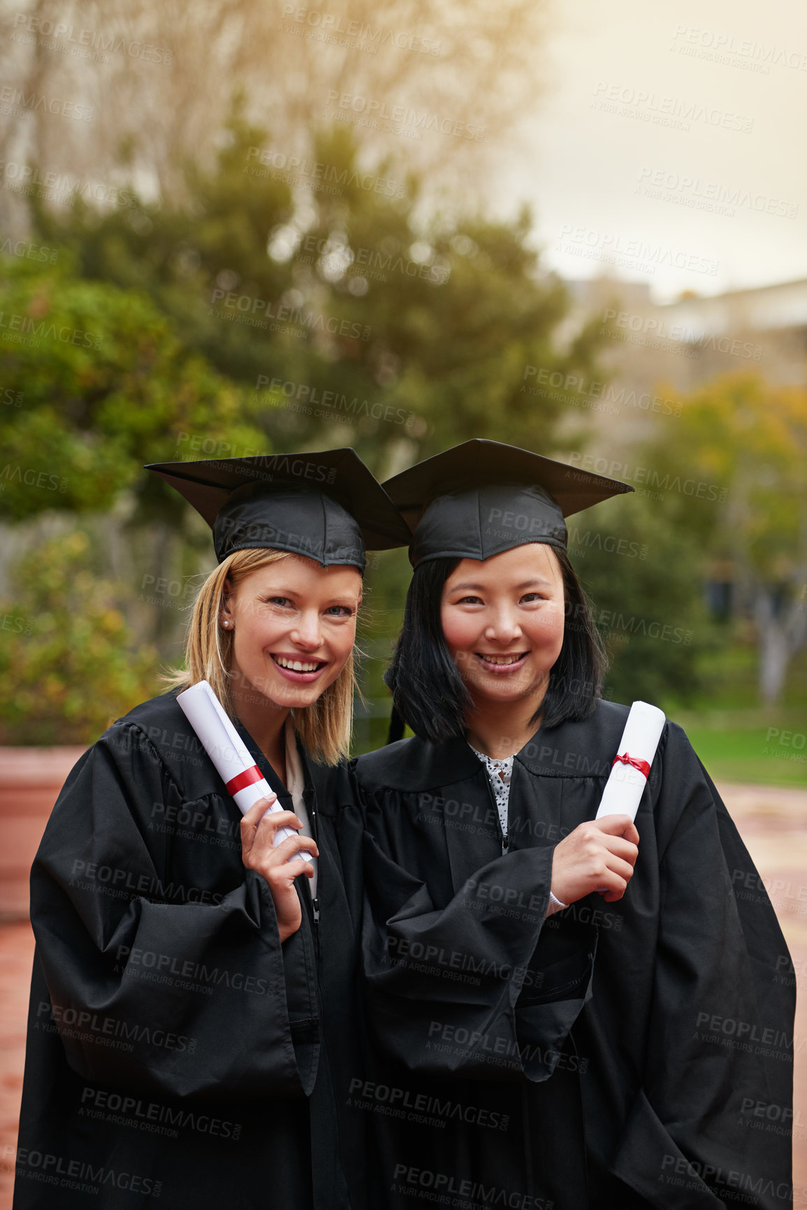 Buy stock photo Shot of two college graduates holding their diplomas