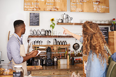 Buy stock photo Woman, cafe and pointing at menu on wall with barista, notes and decision for good customer experience. Male waiter writing, lady and talking with choice, thinking and order special from bakery shop