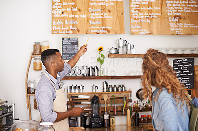Buy stock photo Coffee shop, customer and barista with pointing at menu for purchase, decision and service at restaurant. Waiter, small business and woman at cafe with options, discussion and choice for lunch order