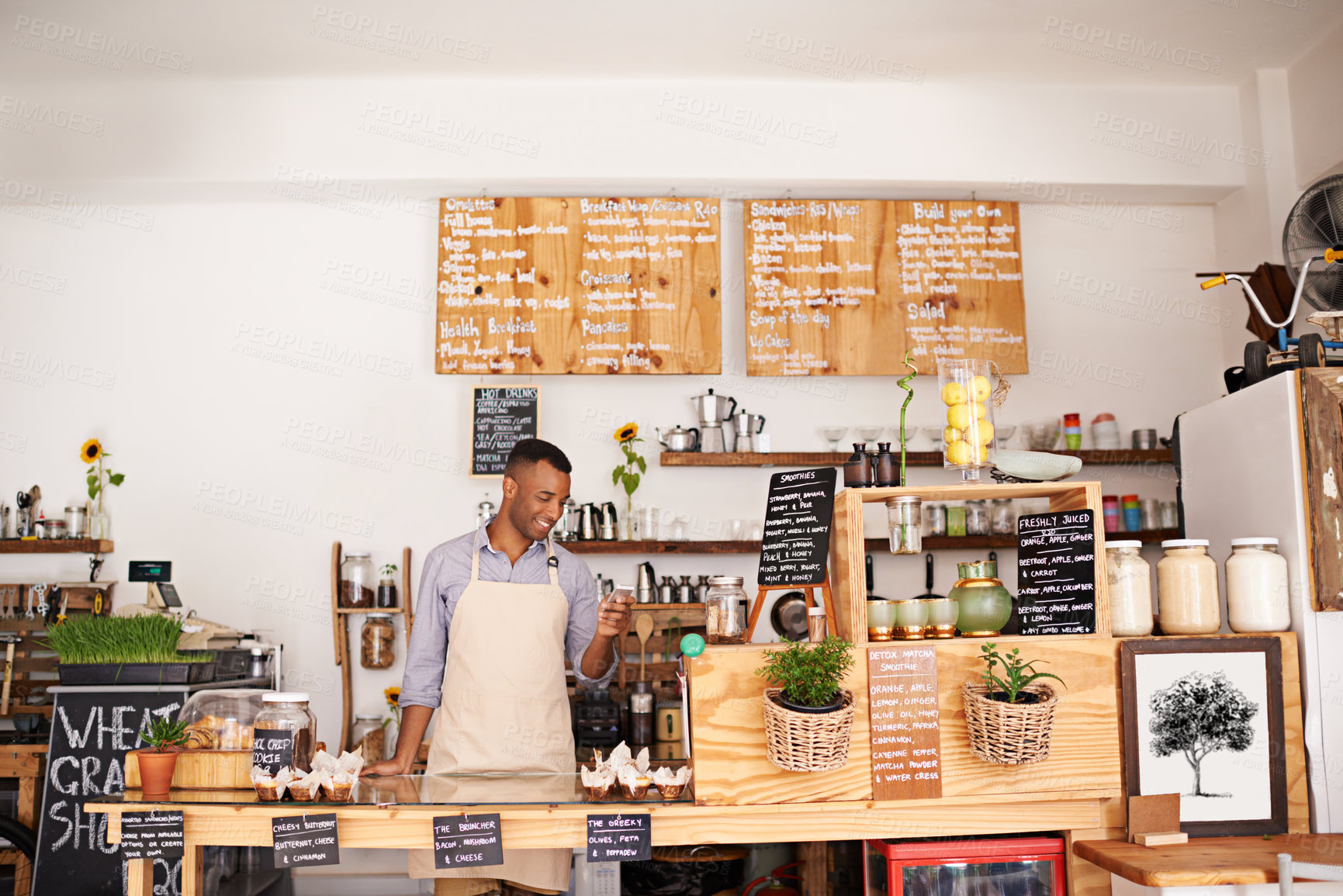 Buy stock photo Black man, coffee shop worker and phone of an entrepreneur with happiness from small business. Cafe, mobile and barista looking on music app for song with smile at bakery and restaurant feeling happy