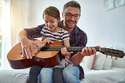 Buy stock photo Shot of a little girl playing the guitar with her father