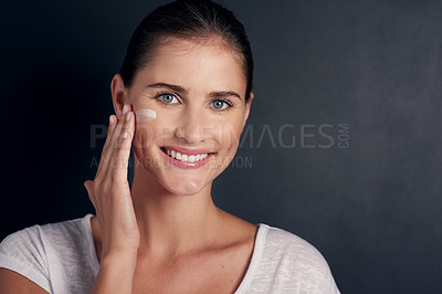Buy stock photo Studio portrait of an attractive young woman applying moisturizer to her face